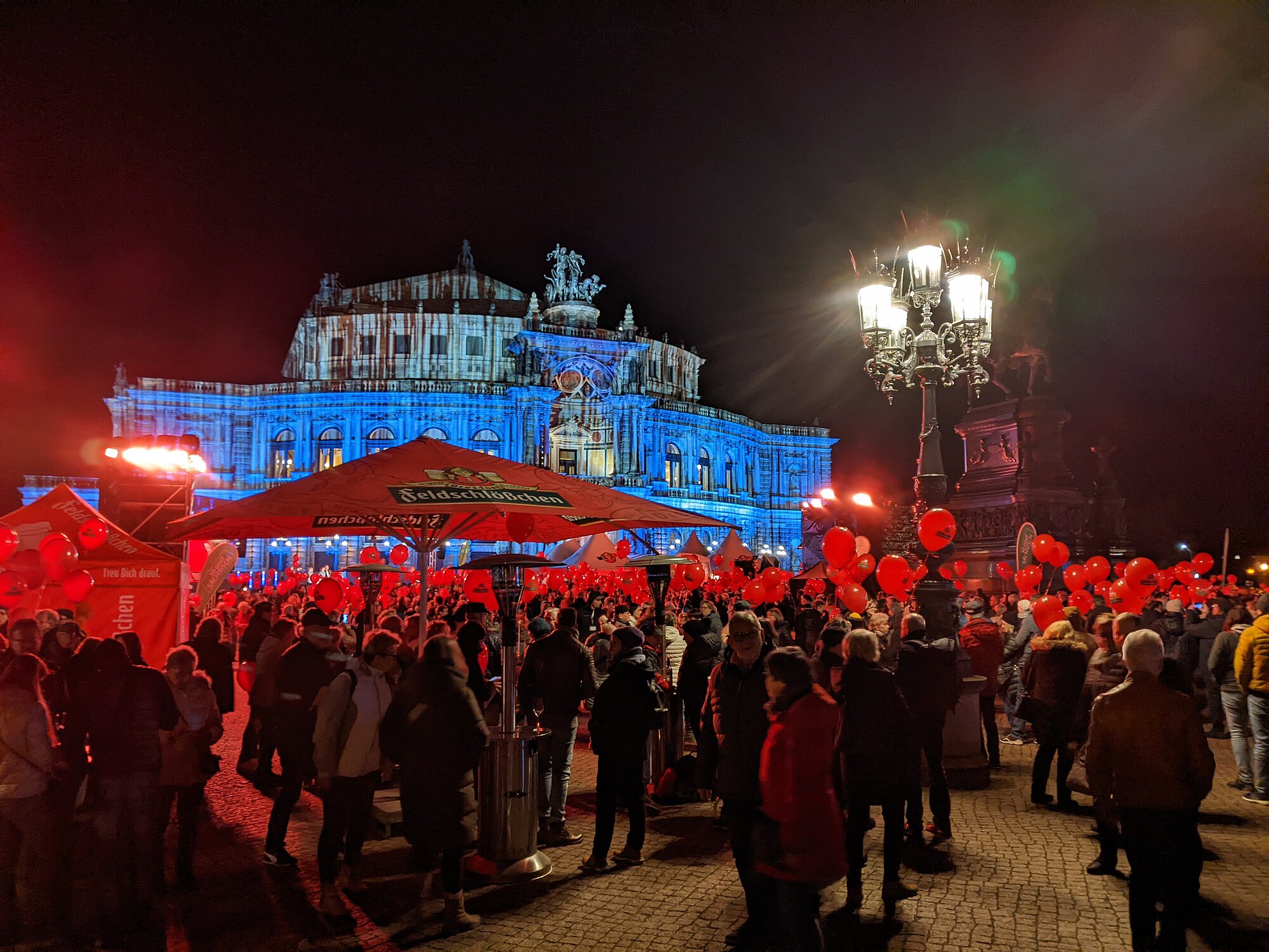 Menschen vor der blau beleuchteten Semperoper mit roten Ballons in der Hand