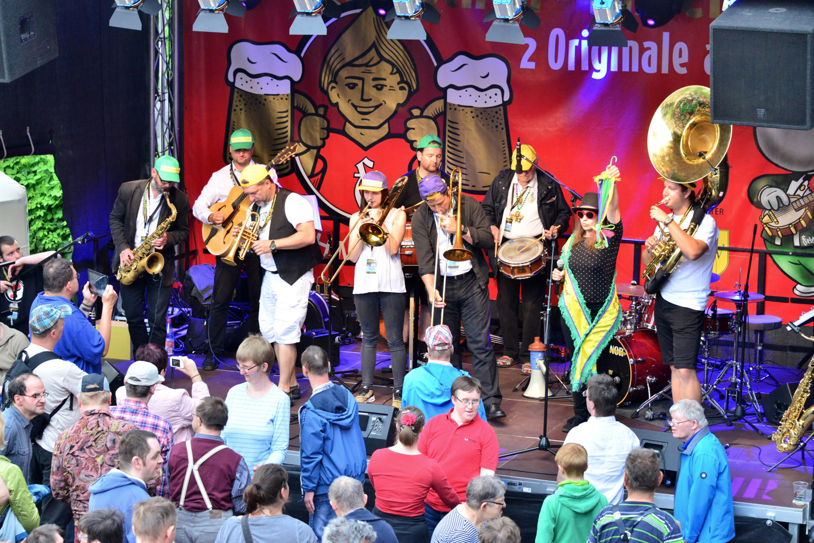 Eine Jazzband spielt auf der Bühne beim Internationalen Dixieland Festival in Dresden, umgeben von einer fröhlichen Menge. Feldschlößchen-Banner schmücken die Bühne im Hintergrund