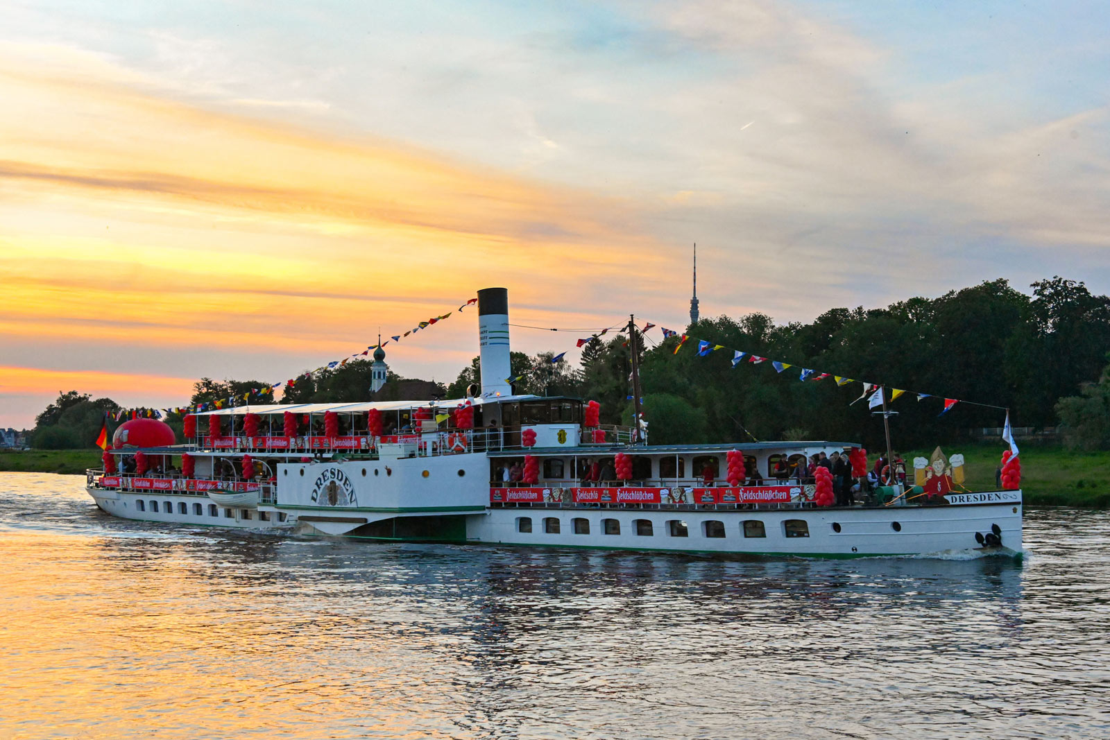 Der in Felschlößchen-rot geschmückte Dampfer auf der Elbe bei Sonnenuntergang.