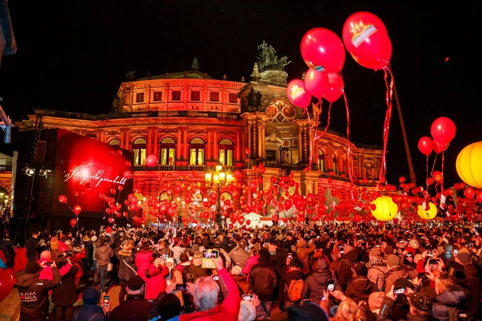 Eine Menschenmenge steht vor der rot beleuchteten Semperoper in Dresden mit roten Luftballons in der Hand